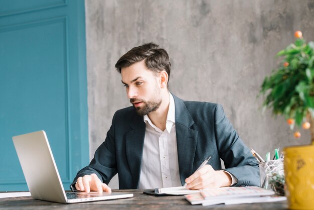 Hombre de negocios usando la computadora portátil y haciendo notas