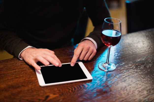 Hombre de negocios usando tableta digital con copa de vino en mostrador