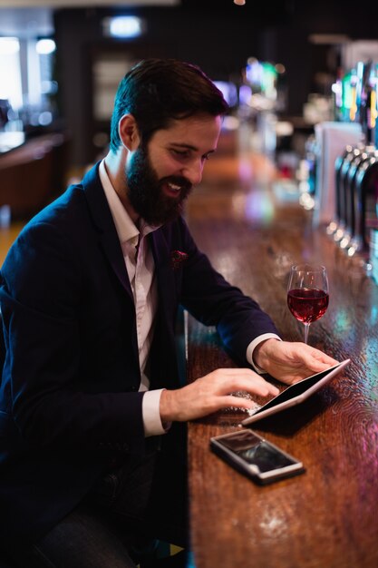 Hombre de negocios usando tableta digital con copa de vino y teléfono móvil en mostrador