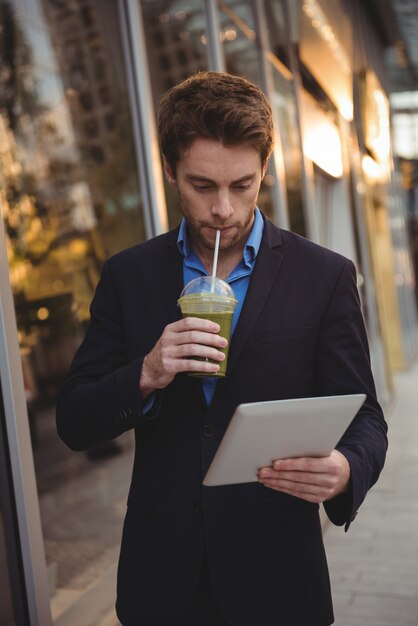 Hombre de negocios usando tableta digital mientras toma jugo