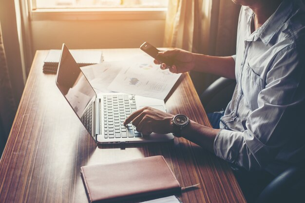 El hombre de negocios utilizando teléfono celular con la computadora portátil en el escritorio de oficina.