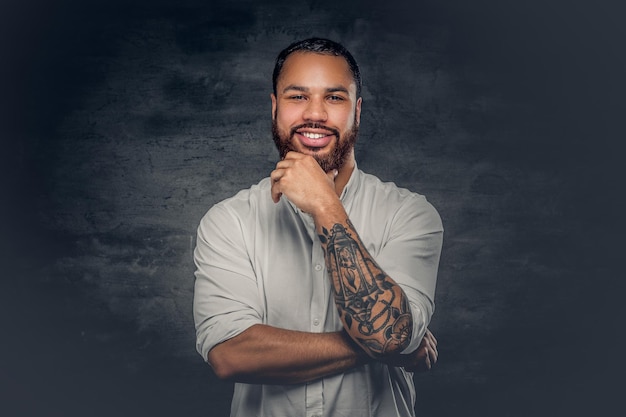 Foto gratuita hombre negro barbudo positivo con un tatuaje en los brazos cruzados, vestido con una camisa blanca.