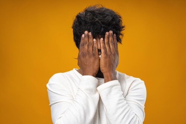 Hombre negro cerrando la cara con las manos contra el fondo amarillo