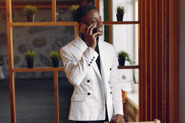 Hombre negro en una chaqueta blanca de pie con un teléfono