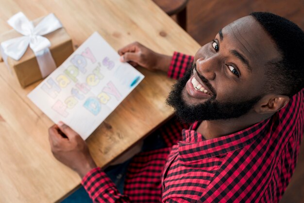 Hombre negro feliz que sostiene la tarjeta de felicitación