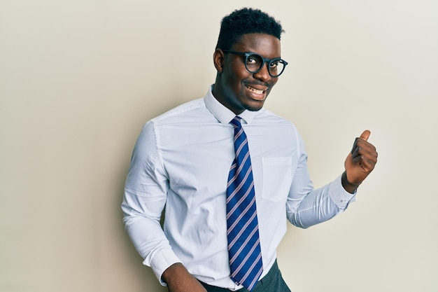 Foto gratuita hombre negro guapo con gafas camisa de negocios y corbata sonriendo con cara feliz mirando y señalando al lado con el pulgar hacia arriba