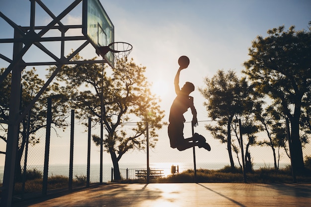 Hombre negro haciendo deporte, jugando baloncesto al amanecer, saltando silueta