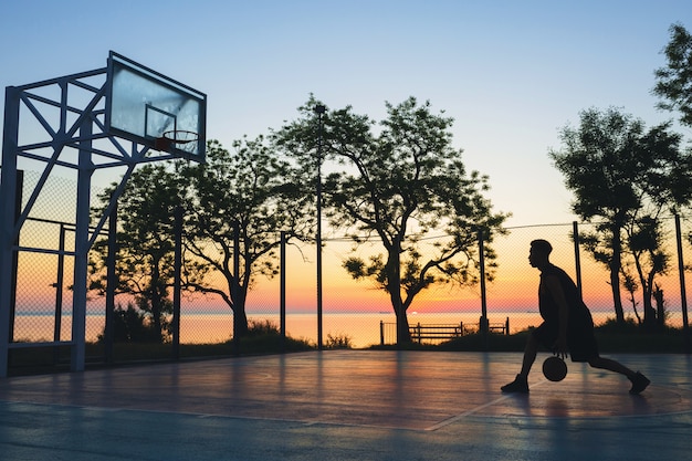 Hombre negro haciendo deporte, jugando baloncesto al amanecer, silueta