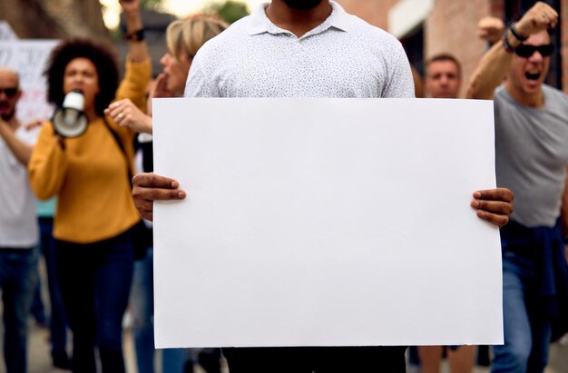 Hombre negro irreconocible protestando con un grupo multiétnico de personas y sosteniendo carteles vacíos Copiar espacio