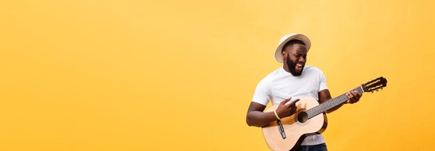 Hombre negro musculoso tocando la guitarra con jeans y camiseta blanca aislada sobre fondo amarillo