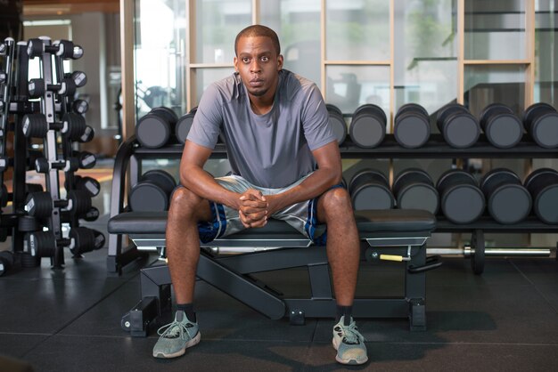 Hombre negro pensativo que se relaja en gimnasio y que mira lejos