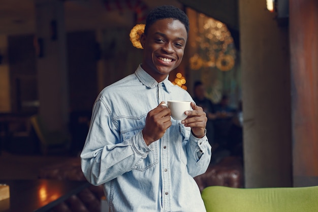 Hombre negro de pie en una cafetería y tomando un café