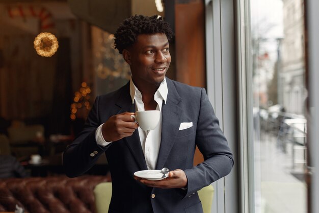 Hombre negro de pie en una cafetería y tomando un café