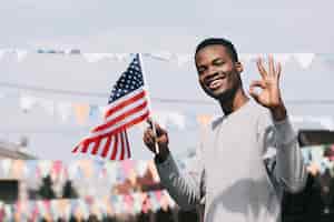 Foto gratuita hombre negro que sostiene la bandera estadounidense y mirando a la cámara con gesto ok