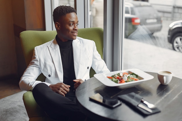 Hombre negro sentado en un café y comiendo una ensalada de verduras