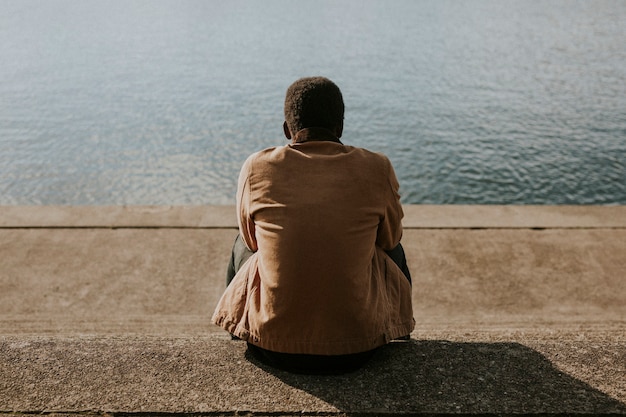 Foto gratuita hombre negro sentado junto al agua