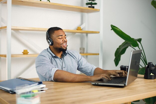 Hombre negro sentado en la oficina usando auriculares y haciendo una videollamada