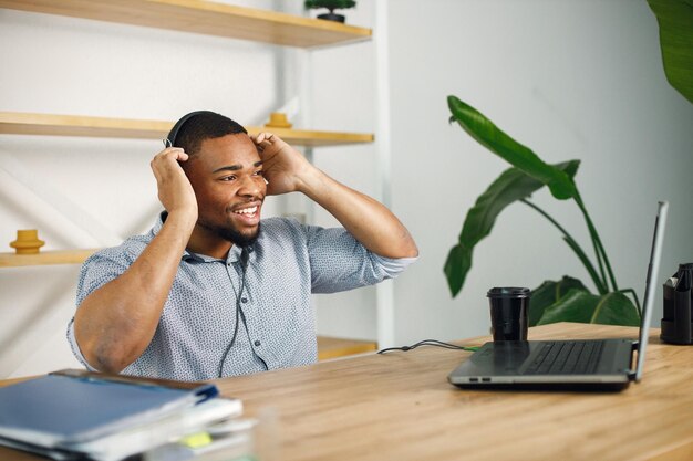 Hombre negro sentado en la oficina usando auriculares y haciendo una videollamada
