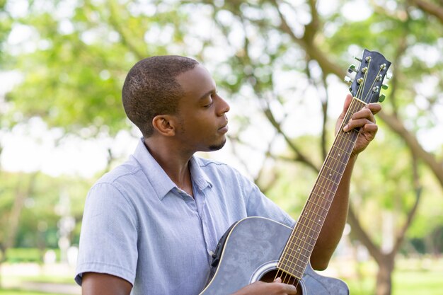 Hombre negro serio que toca la guitarra en el parque