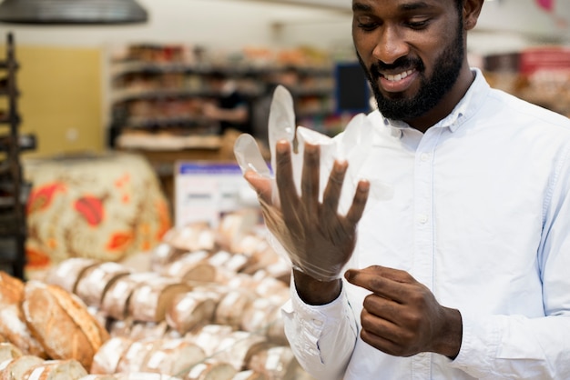 Hombre negro sonriente que pone en guante en la tienda de comestibles para comprar pan