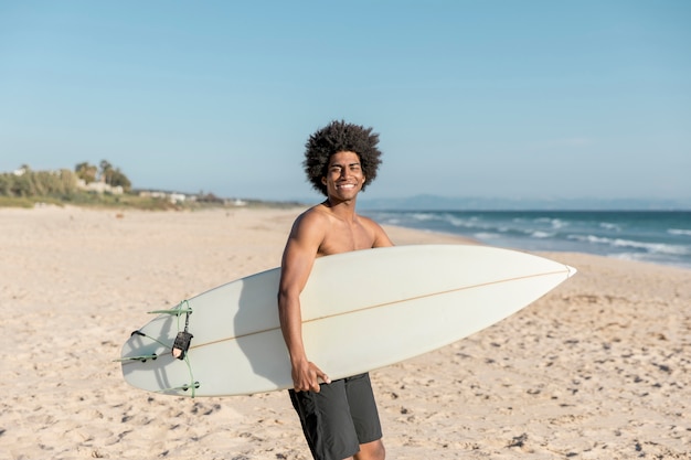 Hombre negro sonriente con tabla de surf en la orilla del mar