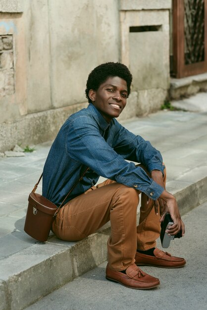 Hombre negro sonriente de tiro completo sentado al aire libre