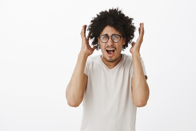 Hombre nerd inseguro en pánico con gafas gritando y estrechándole la mano ansioso