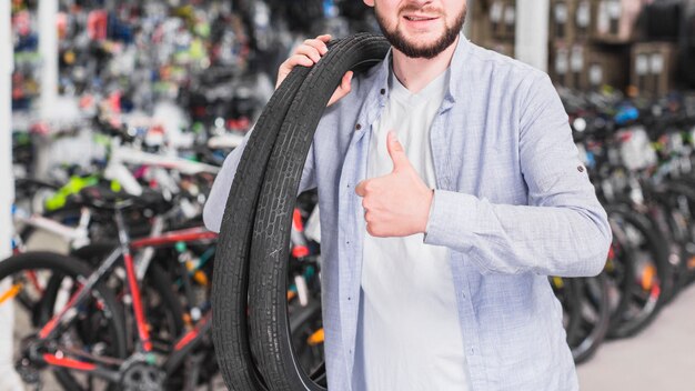 Hombre con neumáticos de bicicleta gesticulando pulgar arriba