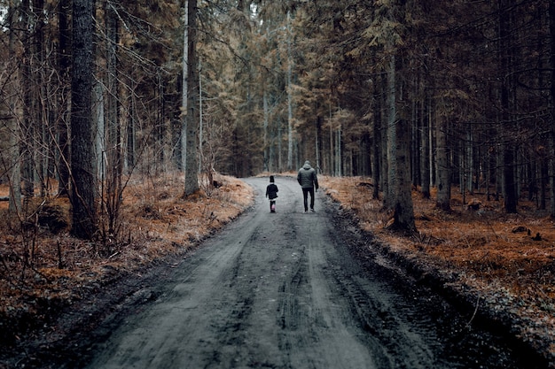 Hombre con un niño caminando por la carretera rodeada por el bosque cubierto de árboles