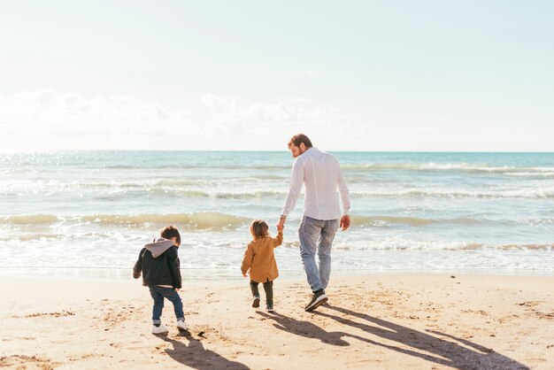 Hombre con niños pequeños caminando hacia el mar