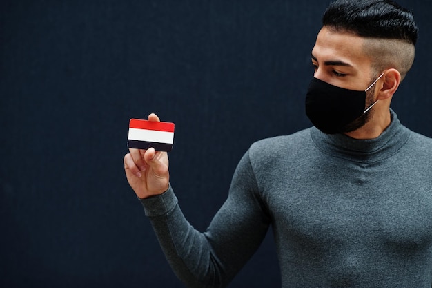 Hombre de Oriente Medio con cuello alto gris y máscara de protección facial negra muestra antecedentes aislados de la bandera de Yemen