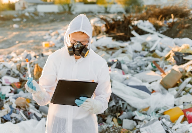 Hombre en overoles en la píldora de la basura. Investigando. Concepto de ecología, contaminación ambiental.