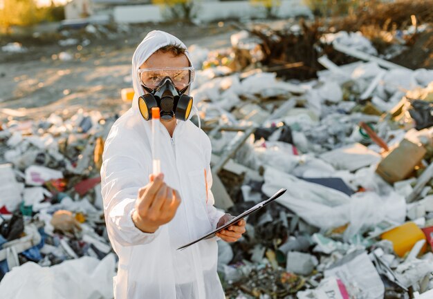 Hombre en overoles en la píldora de la basura. Investigando. Concepto de ecología, contaminación ambiental.