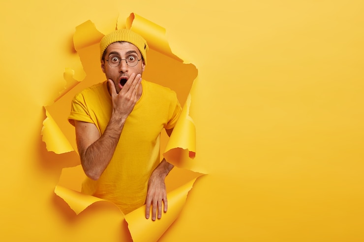 Foto gratuito hombre sin palabras molesto cubre la boca, mira fijamente con ojos saltones, tiene mirada de pánico, vestido con ropa amarilla informal