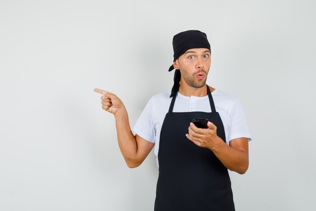 Hombre panadero en camiseta, delantal con teléfono móvil