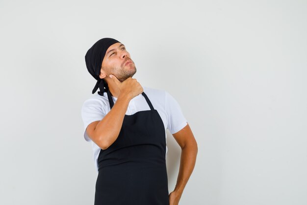 Hombre panadero mirando hacia arriba en camiseta, delantal y mirando pensativo