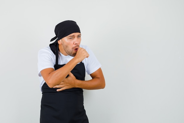 Hombre panadero que sufre de tos en camiseta, delantal y con aspecto de enfermo.