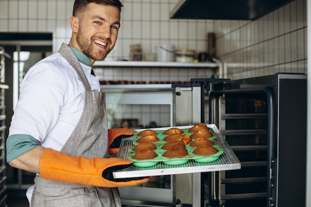 Hombre panadero sosteniendo bollos calientes recién horneados en el horno