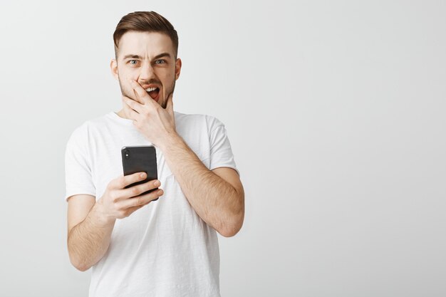 Hombre en pánico sosteniendo teléfono móvil y mirando después de cometer un error