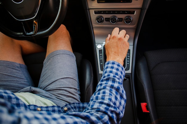 Hombre en pantalones cortos y camisa sentado en el volante sosteniendo la caja de cambios