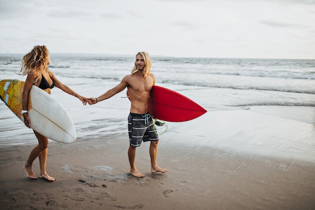 Hombre en pantalones cortos y chica en traje de baño cogidos de la mano. Par va a surfear