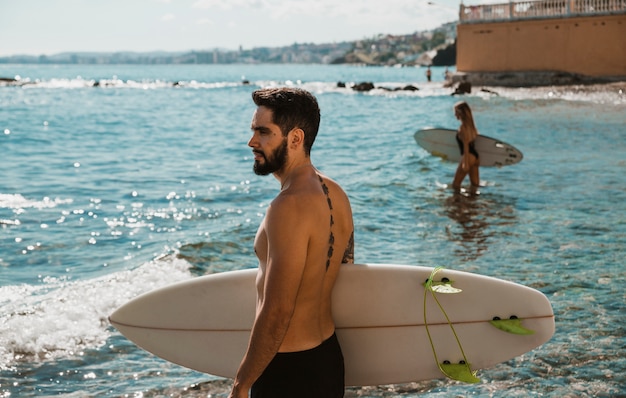 Hombre en pantalones cortos de pie con tabla de surf en el mar