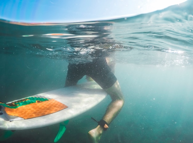 Hombre en pantalones cortos sentado en la tabla de surf en agua azul