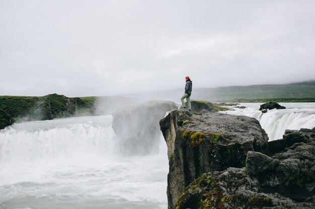 Hombre parado sobre el acantilado de la cascada épica