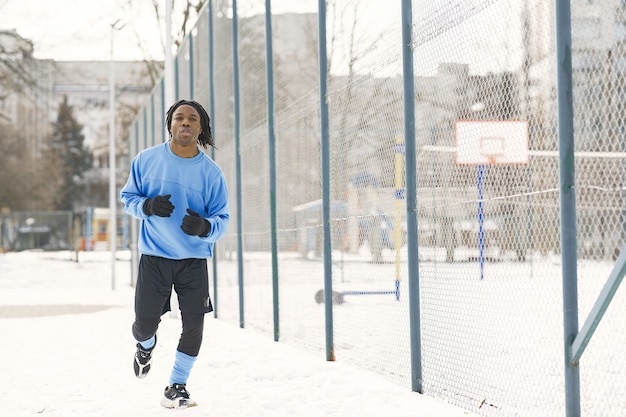 Hombre en un parque de invierno. Chico africano entrenando afuera. El hombre corre.