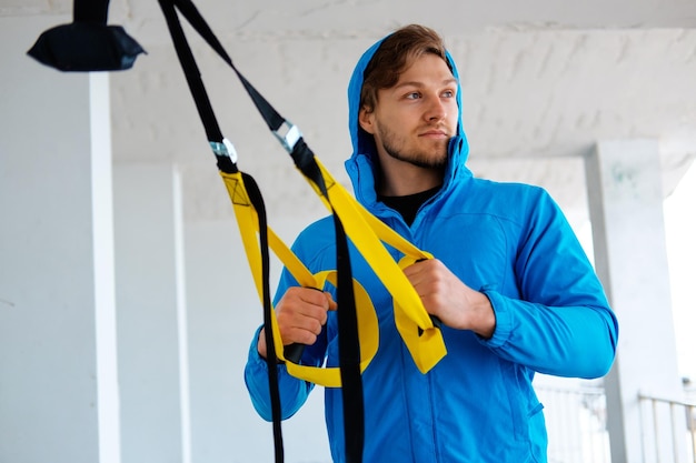 Foto gratuita un hombre en un parque mejorando la flexibilidad de sus piernas con tiras de fitness trx.