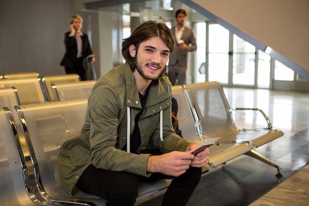 Foto gratuita hombre con pasaporte y tarjeta de embarque sentado en la sala de espera