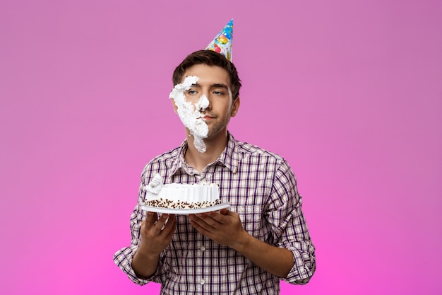 Hombre con pastel en la cara sobre la pared púrpura. Fiesta de cumpleaños.