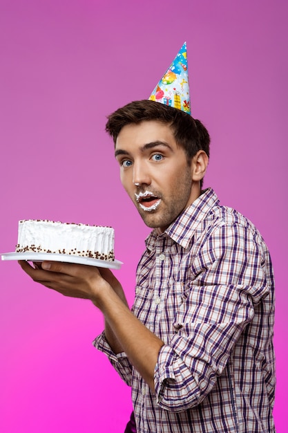 Hombre con pastel en los labios sobre la pared púrpura. Fiesta de cumpleaños.