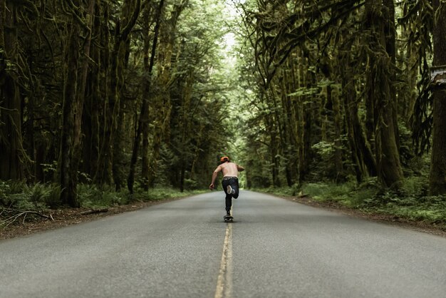 Hombre patinando en una carretera vacía en medio del bosque